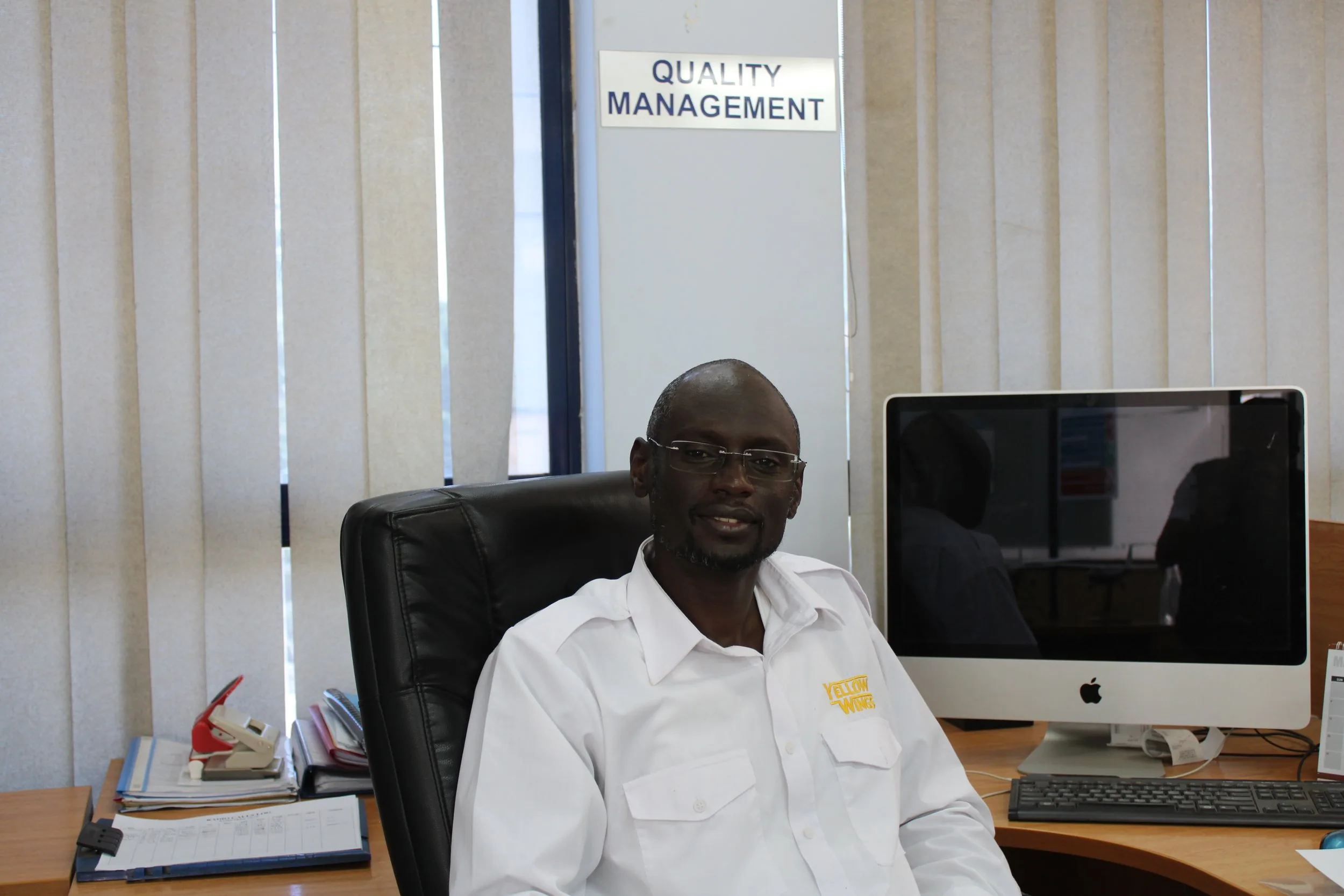 Ibrahim Sebit at his desk under the Quality Management sign.