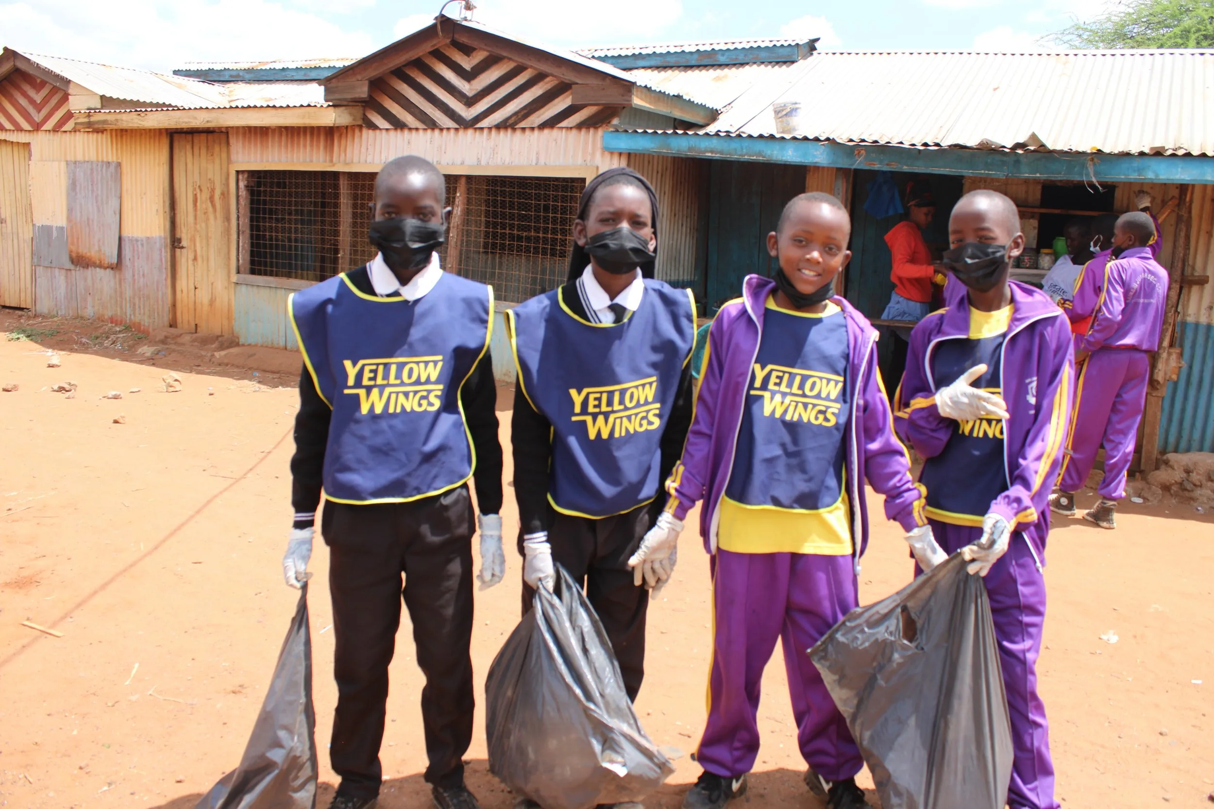 Saikeri clean-up: four pupils in yellow wings bibs with the day's rubbish.