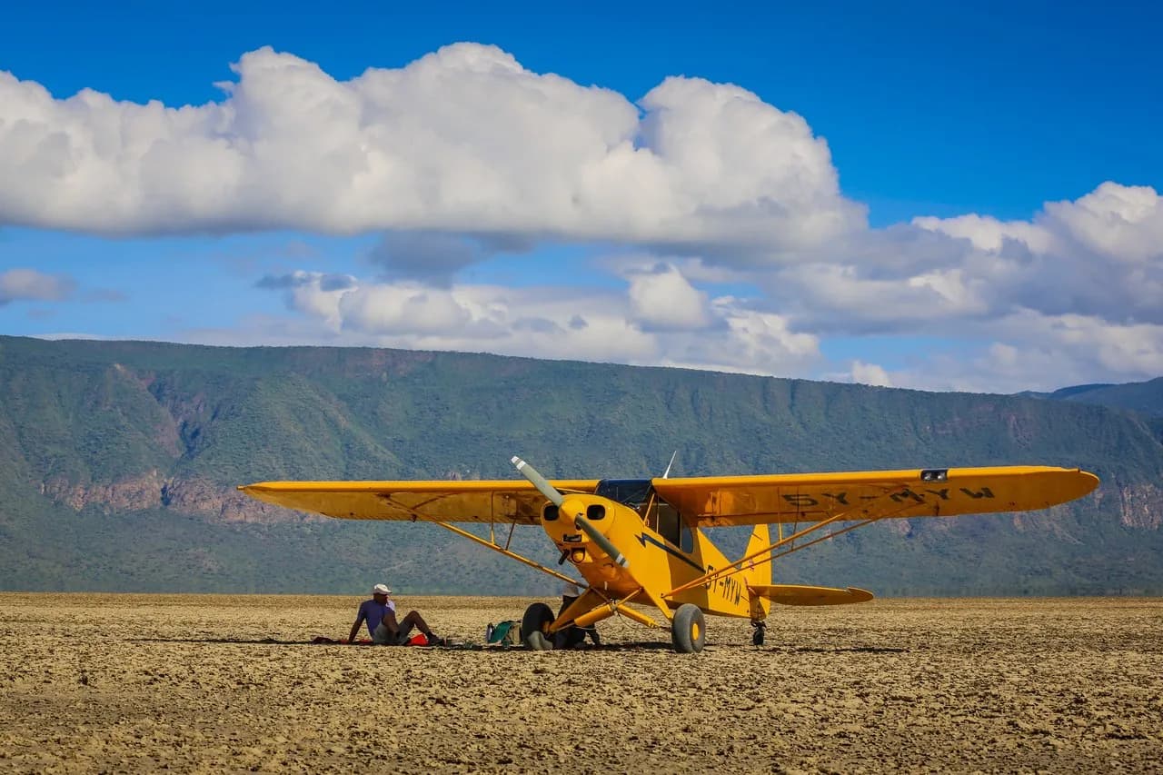 The yellow Piper Super Cub on a dry strip below an escarpment.