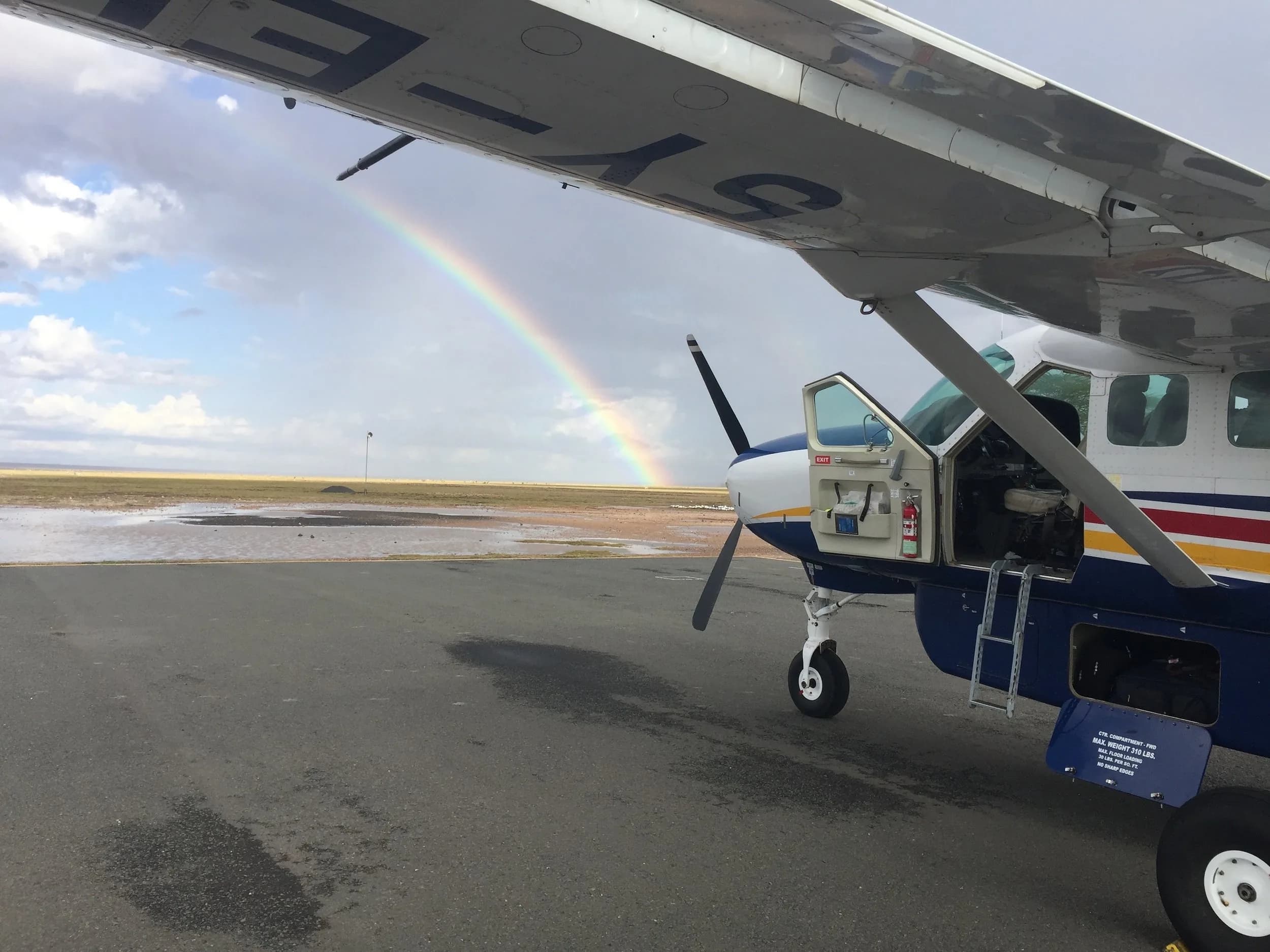 5Y-ELO with its cargo door open, a rainbow over the airfield behind