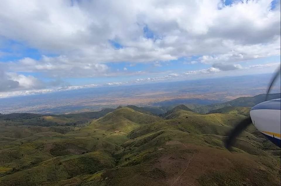 Green hills and a wide plain from the aircraft, the propeller at the edge of the frame