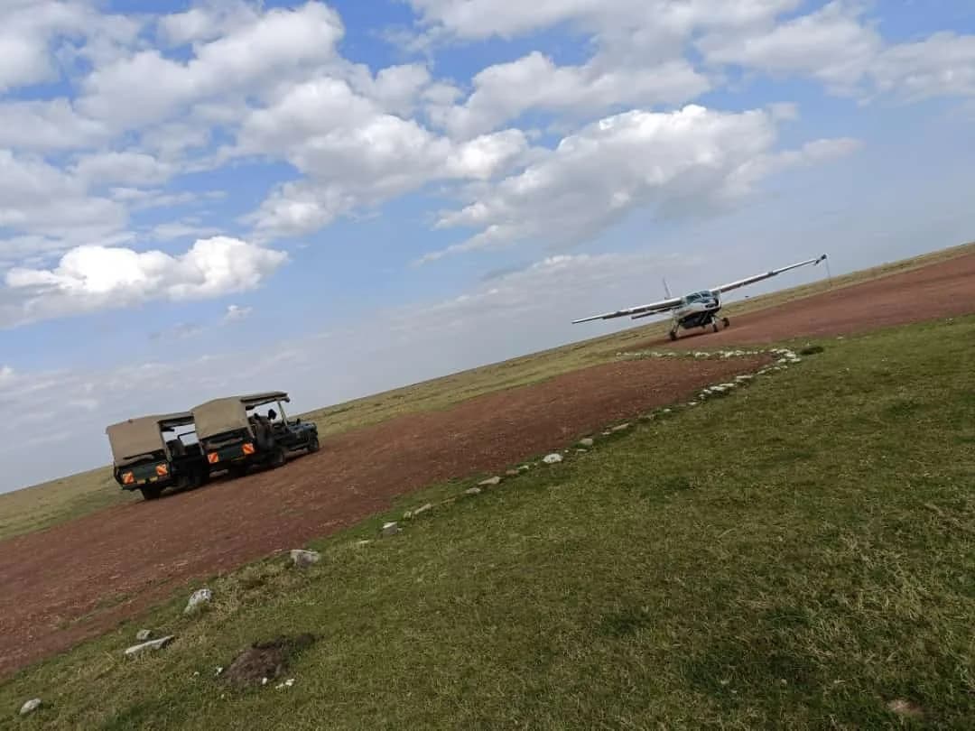 A Yellow Wings Caravan landing on a grass strip in the Masai Mara, a game-drive vehicle waiting